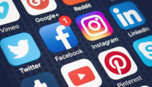 Ein Bildschirm, auf dem verschiedene Social Media Symbole angezeigt werden, darunter vimeo google plus reddit twitter facebook instagram linked in tumblr youtube pinterest und skype, ansicht von schräg oben, in der mittleren reihe befinden sich zentral twitter facebook instagram und linked in, bei facebook ist eine weiße eins in einem roten kreis