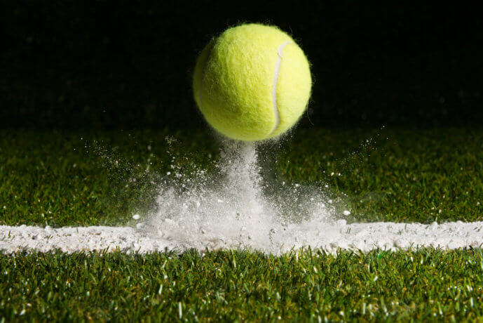 Tennisball prallt von weißer Linie auf grünem Rasen ab.