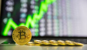 bitcoin-münze-steht-neben-liegenden-bitcoin-münzen-vor-einer-chart-mit-grünem-pfeil-nach-oben