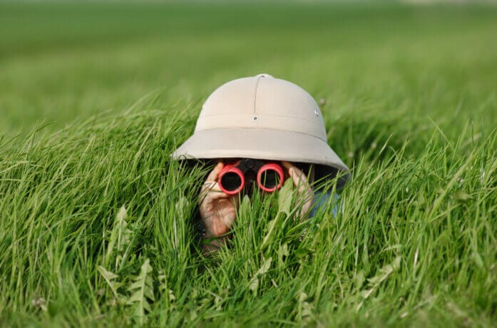 Ein kleiner Junge mit Safari-Hut und Sonnenbrille lauert im hohen Gras