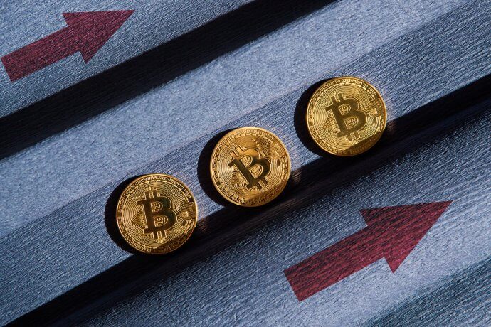 drei goldene bitcoin-münzen, daneben zwei rote pfeile, die nach rechts oben zeigen