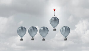 fünf graue heißluftballons, von denen sich der vierte von links von den anderen abhebt, indem er von einem roten kleineren ballon nach oben gezogen wird