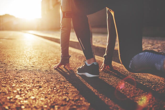 Läufer in Startposition und Sonne scheint entgegen auf Straße