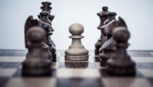 Auf einem Schachbrett ist ein Bauer von anderen Spielfiguren umzingelt, die institutionelle Investoren darstellen sollen.