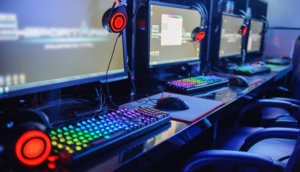 Mehrere Gaming-Computer stehen in einem Internetcafe nebeneinander und die Tastaturen leuchten bunt.