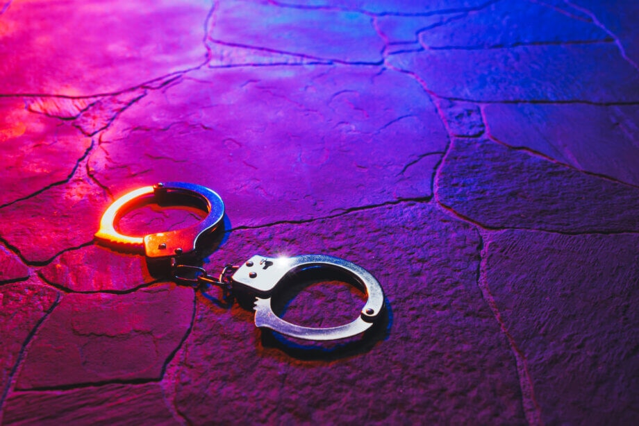 Bitcoin-Abzocken: Chinesische Polizei ermittelt gegen Scam-Exchange Handschellen, die vor einem blau-violetten Hintergrund liegen