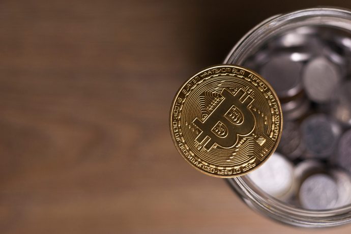 Bitcoin-Münze liegta auf dem Rand eines Glases voller Kleingeld