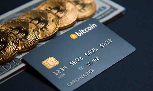 Binance-Card-Gerüchte ziehen Swipe-Kurs durch die Manege Kreditkarte mit Aufschrift Bitcoin liegt vor mit Bitcoin-Münzen bedecktem Dollarschein