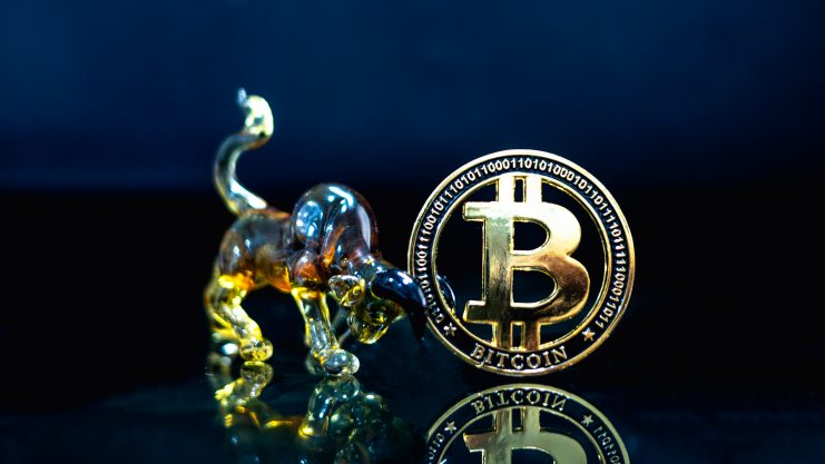 Bitcoin-Münze neben Bullen-Figur aus Glas