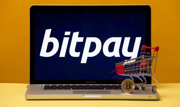 (Günstiger)Bezahlen mit Bitcoin: BitPay führt SegWit ein Laptop mit Bitpay-Logo auf dem Bildschirm und Miniatur-Einkaufswagen samt Bitcoin-Münue