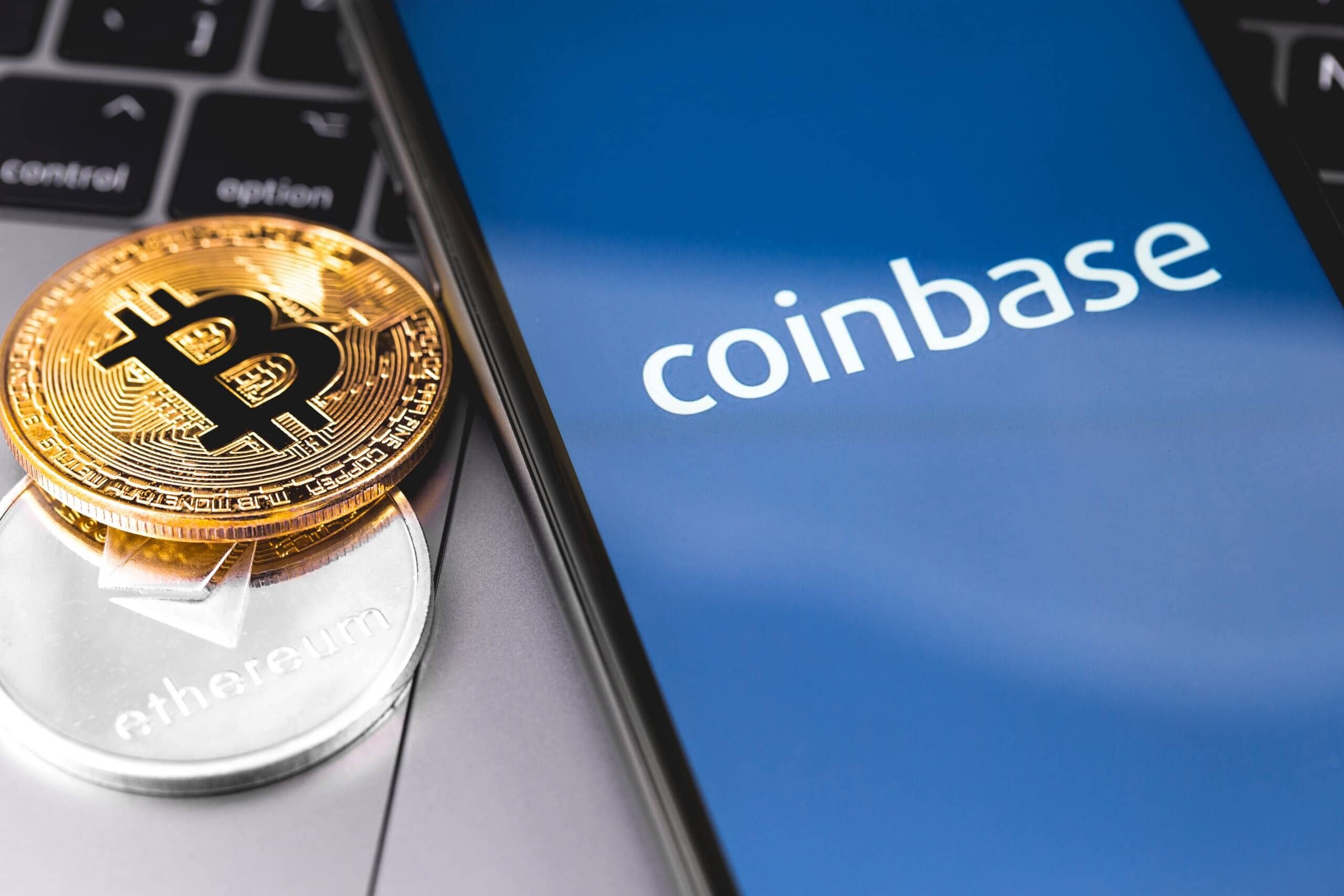 Bitcoin- und Ethereum-Münzen neben Smartphone mit Coinbase-Logo auf dem Bildschirm