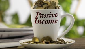 Zum Überquellen mit Münzen befüllte Kaffeetasse mit dem Aufdruck „Passive Income“ (Passives Einkommen)