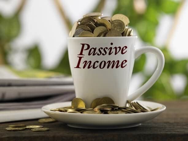 Zum Überquellen mit Münzen befüllte Kaffeetasse mit dem Aufdruck „Passive Income“ (Passives Einkommen)