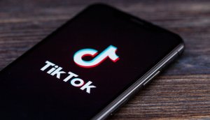 das symbol der tiktok app auf einem schwarzen smartphone, das auf einem braunen holztisch liegt