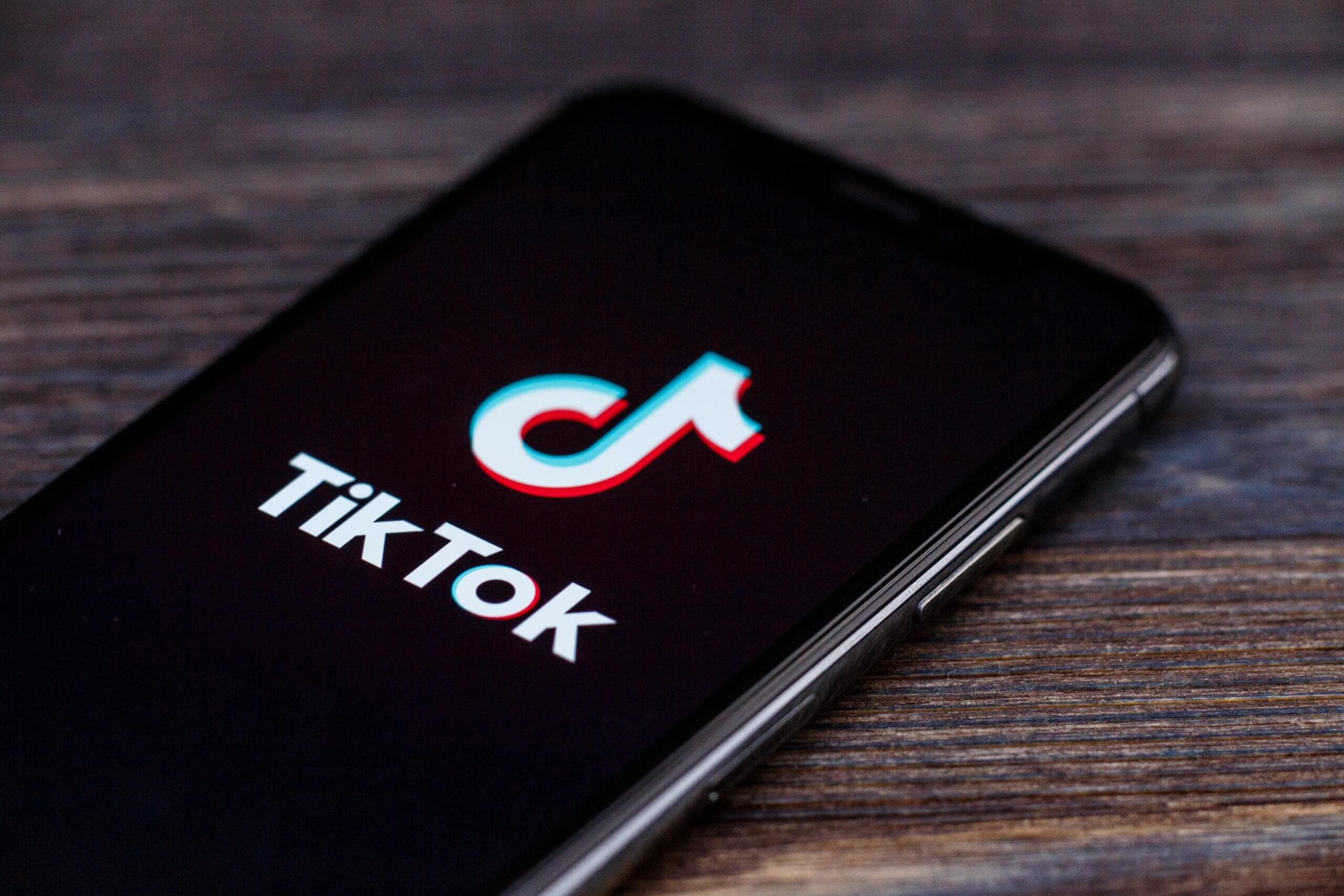 das symbol der tiktok app auf einem schwarzen smartphone, das auf einem braunen holztisch liegt