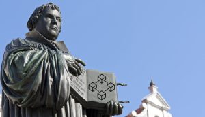 Das Bild zeigt eine Statue Martin Luthers, der seine Thesen präsentiert.