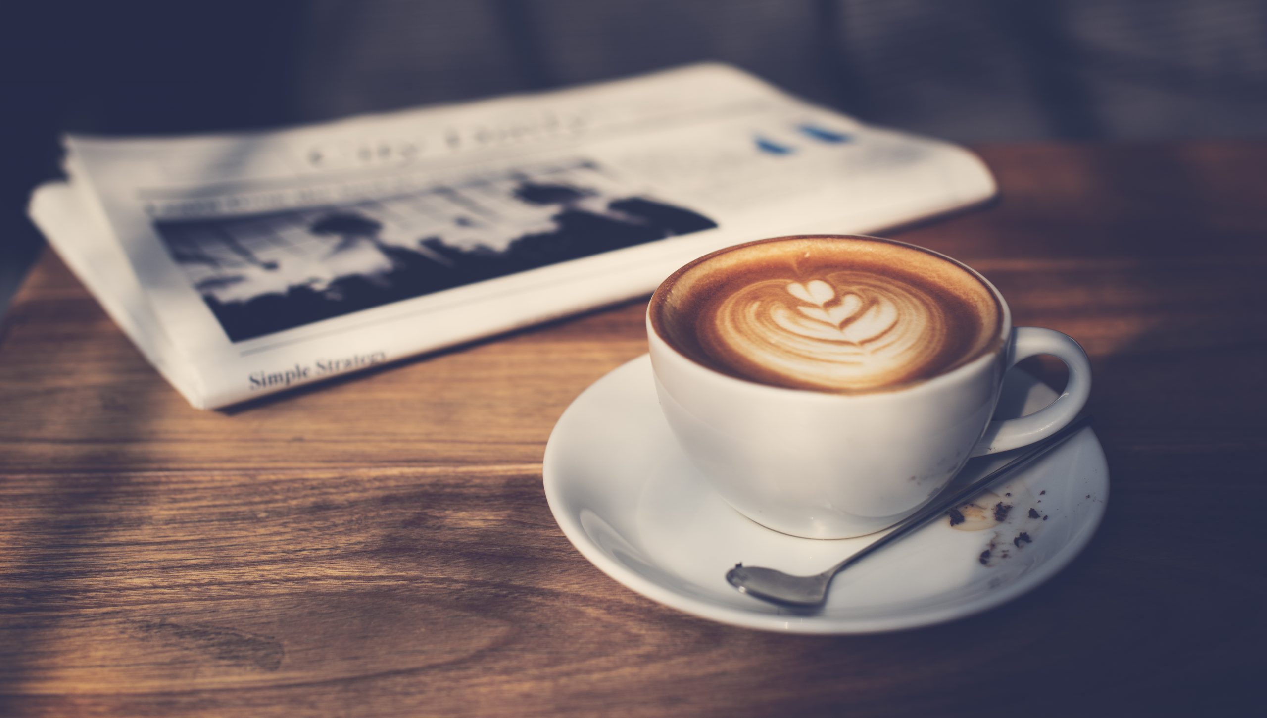 Dekorativer Kaffee mit Latte-Art vor zusammengefalteter Zeitung auf Holztisch.