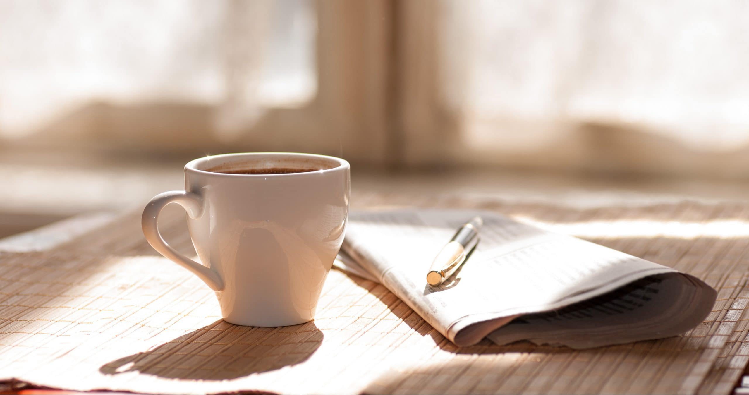 kaffeetasse-neben-einer-zeitung-auf-einem-holztisch