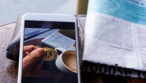 Morning news cryptocurrency with newspaper and bitcoin on mobile screen.