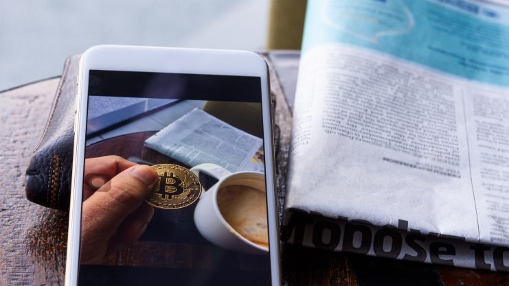 Morning news cryptocurrency with newspaper and bitcoin on mobile screen.