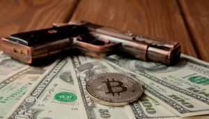 Black pistol, dollars and coin in the form of bitcoin on wooden background.