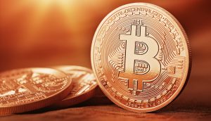 Physische Repräsentanz einer Bitcoin-Münze auf güldenem Hintergrund.