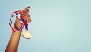 Frau, die Hand hob, hielt Goldmedaille gegen den Himmel. Preis- und Siegeskonzept