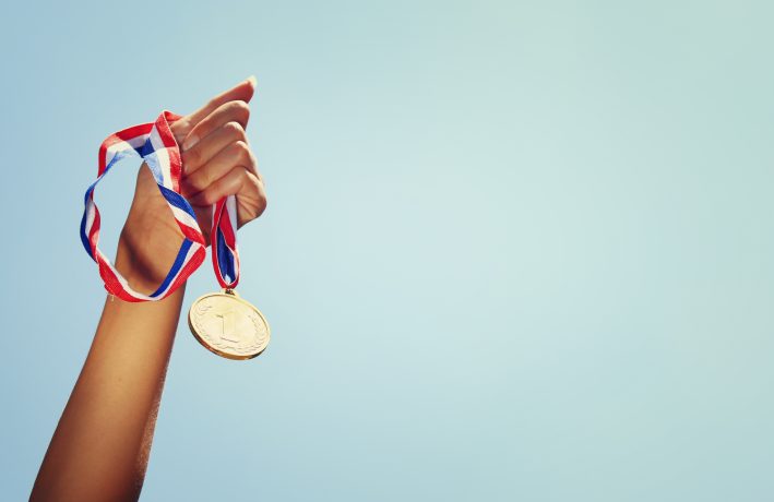 Frau, die Hand hob, hielt Goldmedaille gegen den Himmel. Preis- und Siegeskonzept