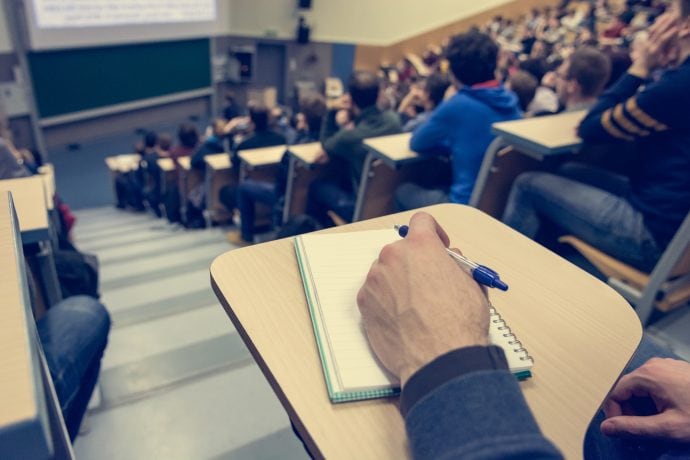 Hörsaalgebäude in dem Studenten sitzen und mitschreiben.