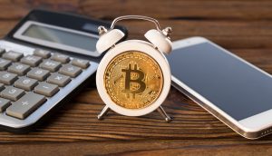 Kleiner Wecker mit Bitcoin zwischen Taschenrechner und Smartphone