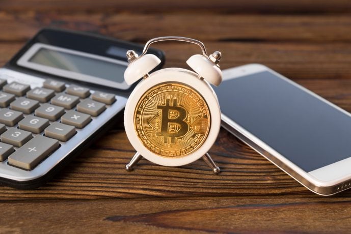 Kleiner Wecker mit Bitcoin zwischen Taschenrechner und Smartphone