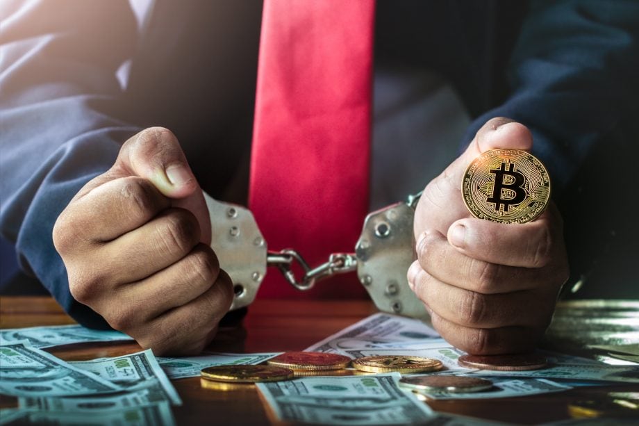 Schlag gegen Darknet-Märkte: 179 Drogendealer wandern hinter Gitter Mann in Handschellen, in der Linken hält er eine Bitcoin-Münze