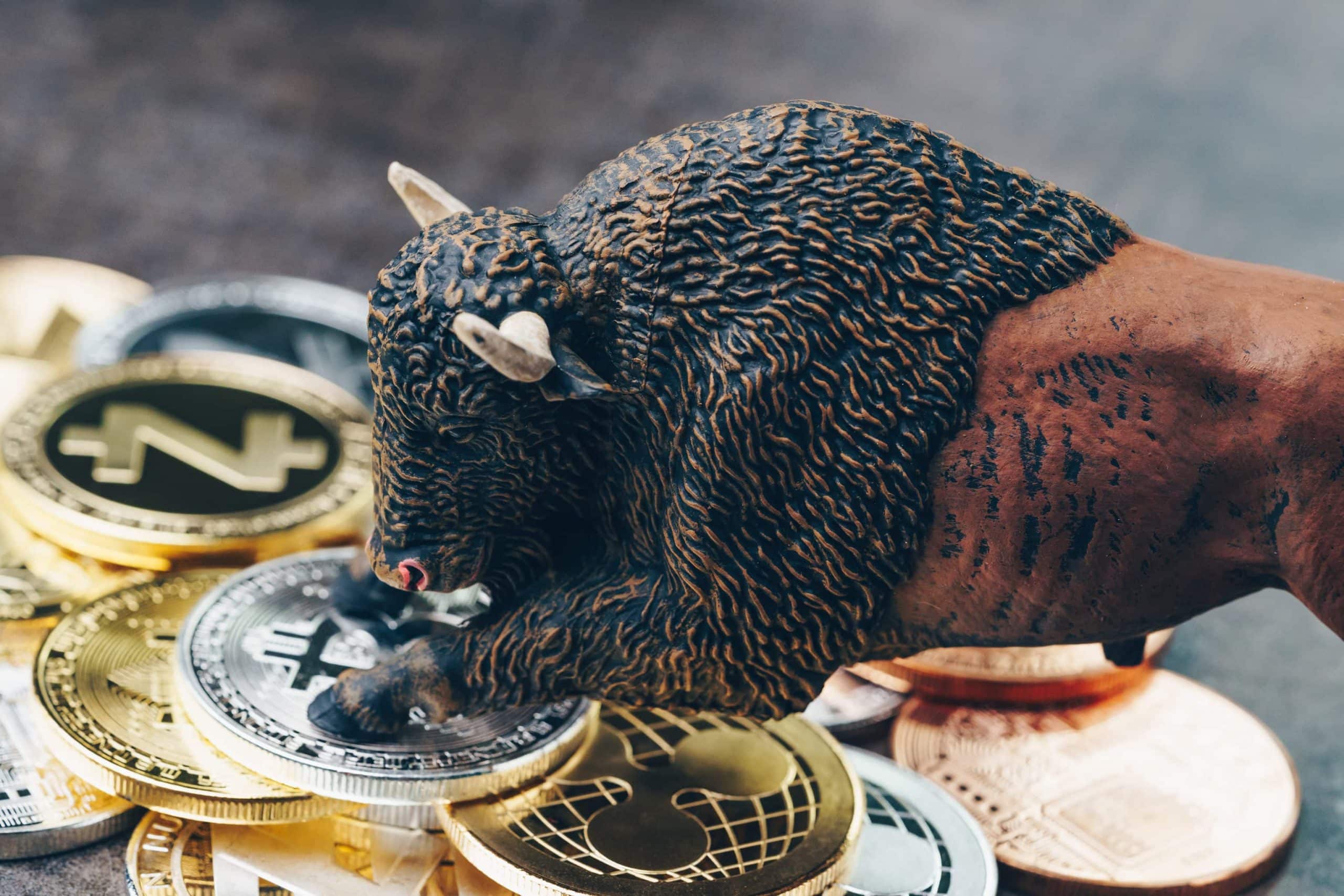 Eine Bullenfigur steht mit den Vorderläufen auf einem Stapel von Bitcoin- und Altcoin-Münuen