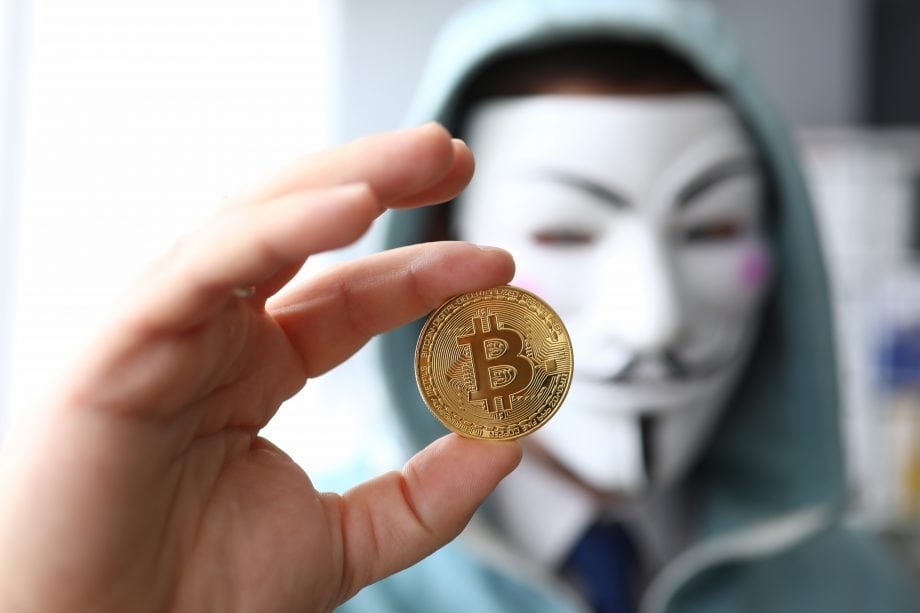 Bitcoin Mixer Helix in Erklärungsnot: 60 Millionen US-Dollar Strafe festgesetzt Bitcoin Münze wird von Menschen mit Maske hochgehalten.