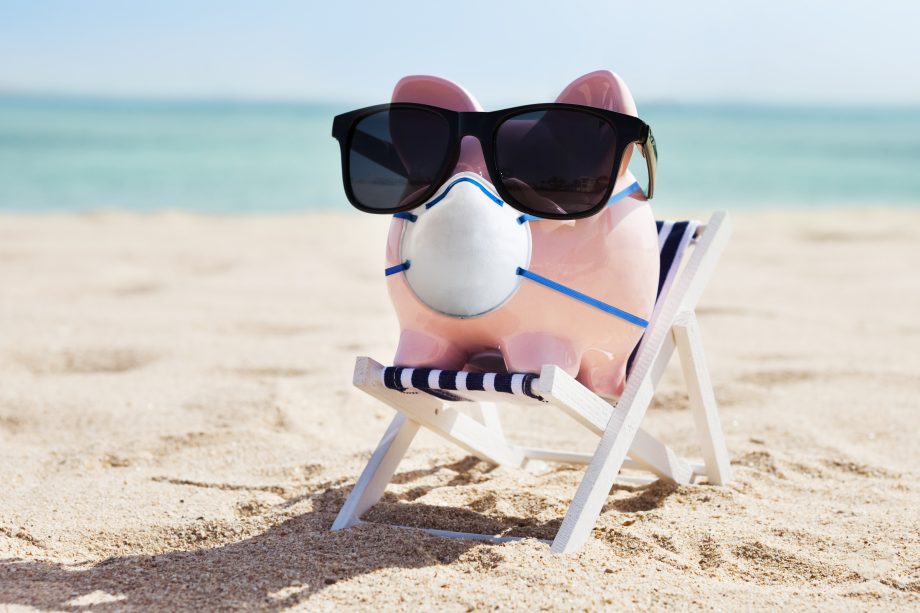 Passives Einkommen: Verdoppele dein Geld während Covid-19 Ein Sparschwein mit Mund-Nasen-Schutz und Sonnenbrille auf einer Liege am Strand