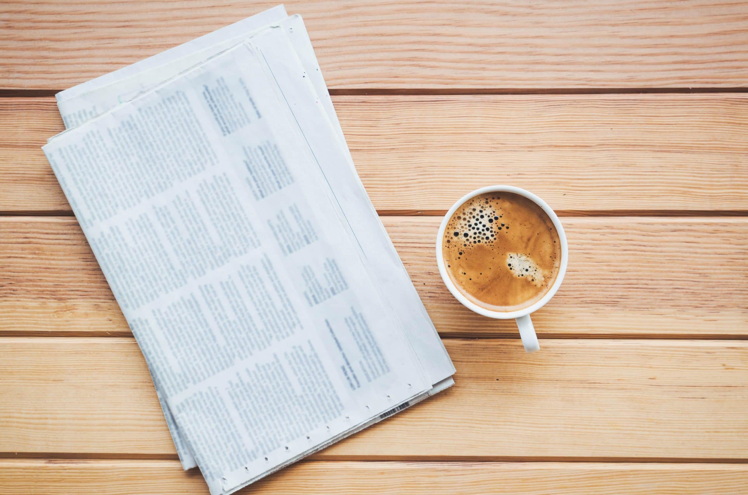 Eine Zeitung liegt zusammen mit einer Kaffeetasse auf einem Tisch.