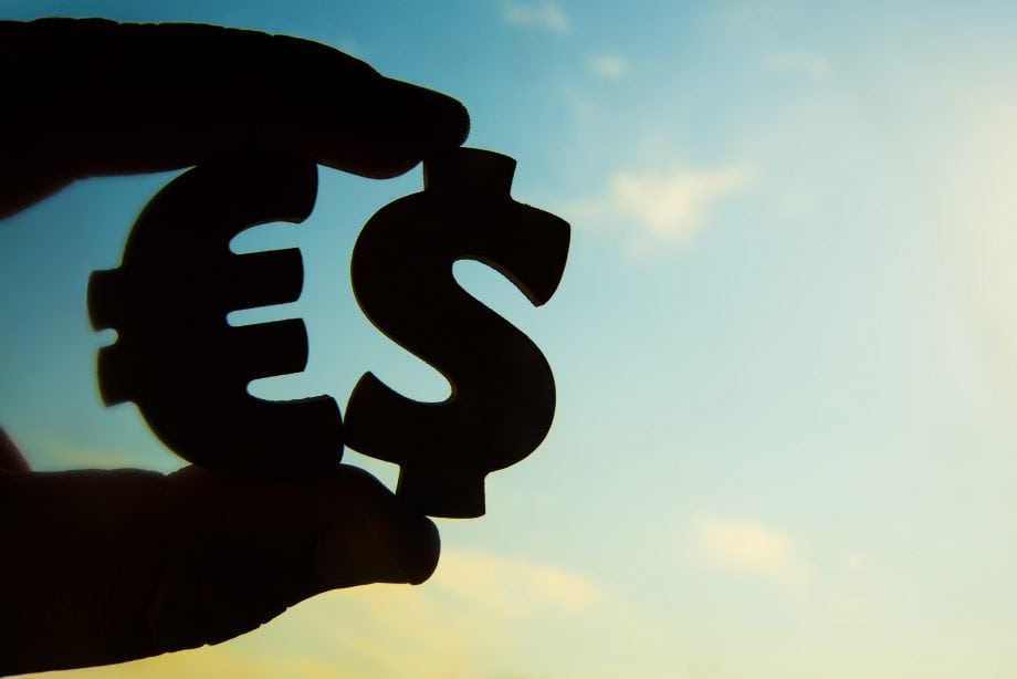 Regulierungs-ECHO: Wann kommt der digitale Euro? Im Gegenlicht fotographierte Aufnahme einer Hand, die ein Euro- sowie ein Dollar-Zeichen hält