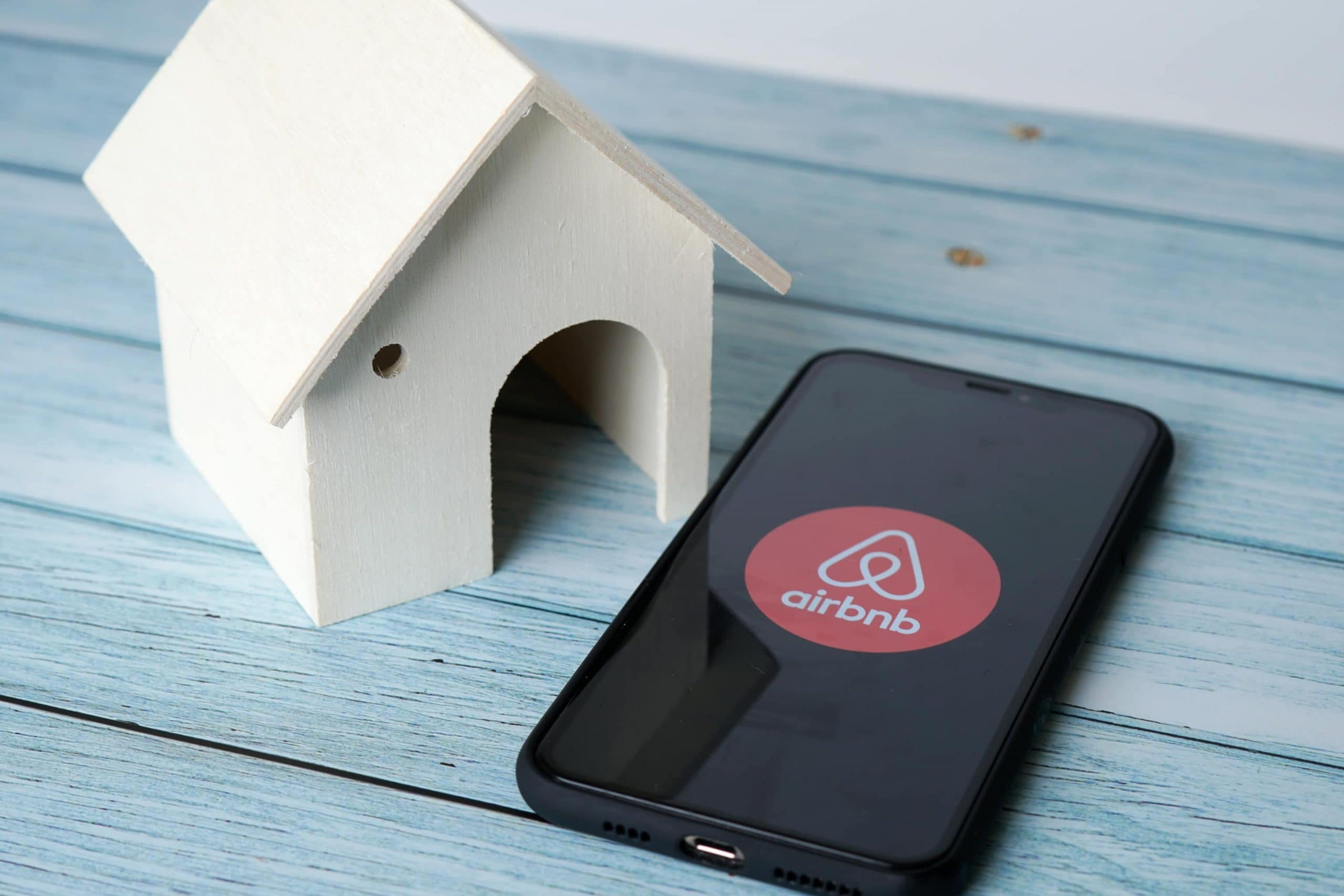 Smartphone mit Airbnb Logo liegt auf einem Tisch neben einem Miniaturhaus