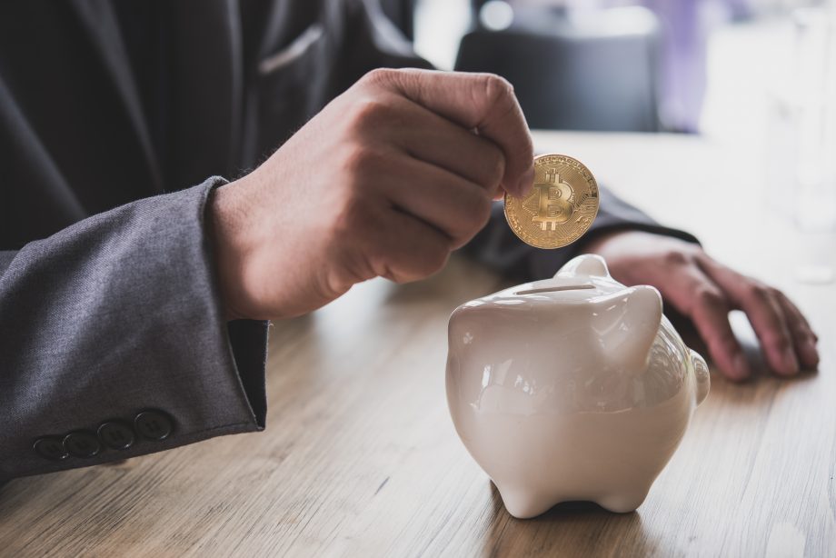 Traden war gestern: Wie man mit My-Masternode passives Einkommen generiert Person steckt Bitcoin-Münze in ein Sparschwein