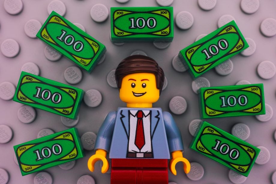 DeFi: Potenzial für „ETF-Token“ ist gigantisch – Welche Projekte gibt es? Lego-Männchen umringt von Lego-Geldscheinen auf grauer Bodenplatte
