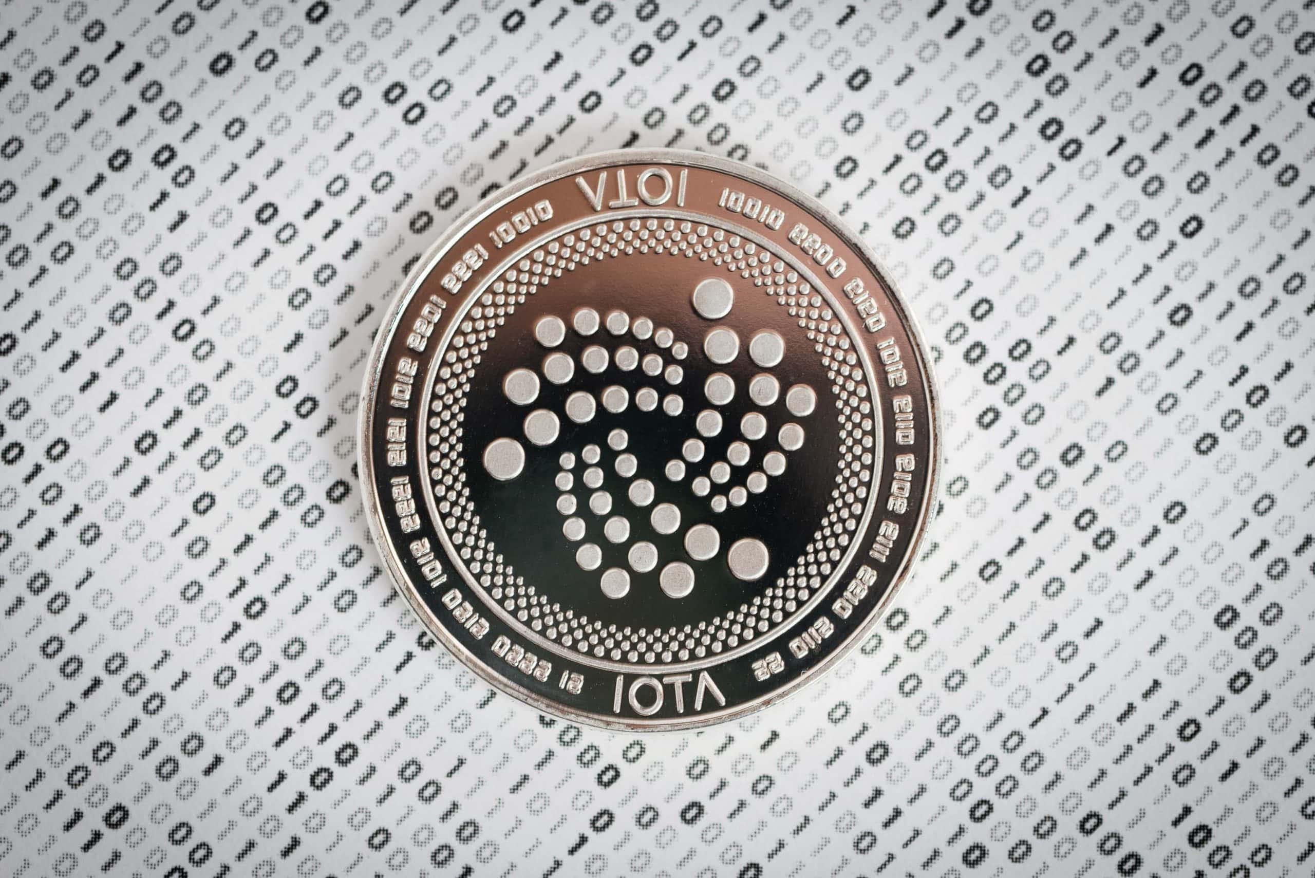 IOTA-Münze auf Papier, das mit Nullen und Einsen bedruckt ist