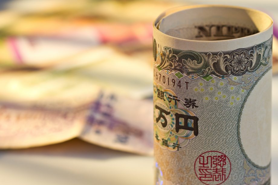 Japan: 30 Großunternehmen kündigen neues Zahlungssystem an Eine zusammengerollte Yen-Note, im Hintergund weitere Geldscheine