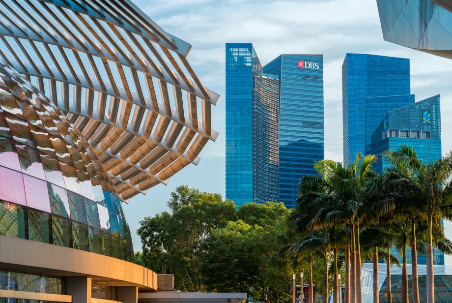 DBS Digital Exchange: DBS kündigt eigene Börse für digitale Assets an. Man sieht eine Palmenallee. Am Horizont sind mehrere Wolkenkratzer, auf einem ist das DBS-Logo zu sehen.