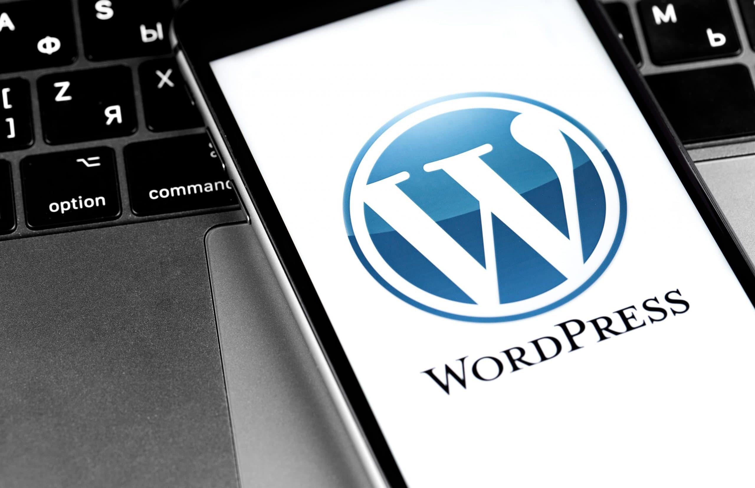 Man sieht das WordPress-Logo auf einem Smartphonebildschirm, das auf einer Laptoptastatur liegt. auf einem