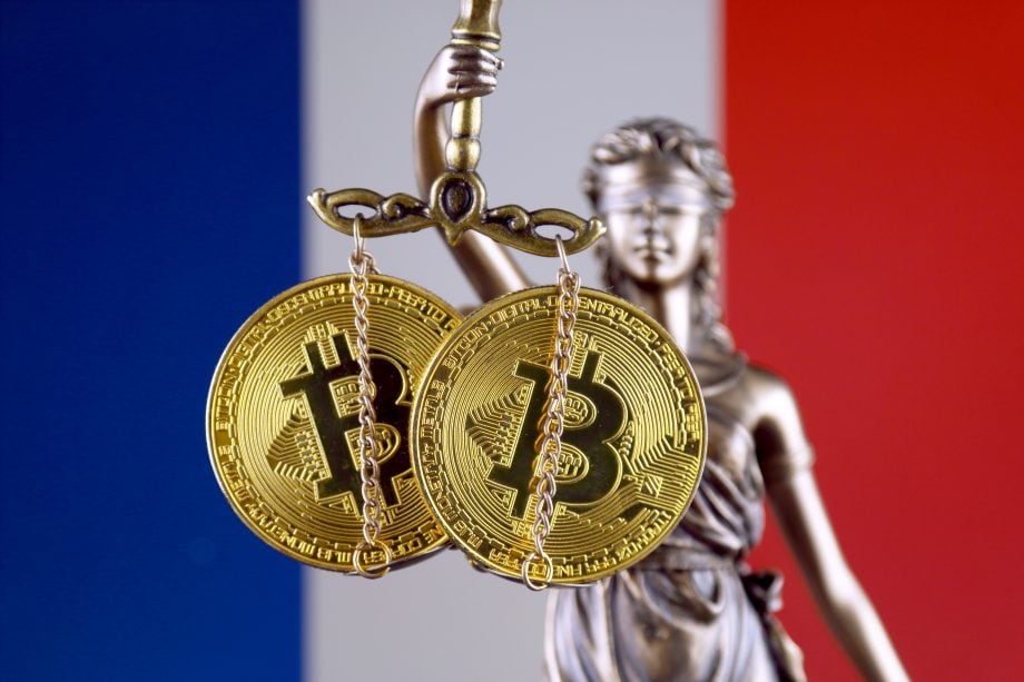 Frankreich stellt strenge KYC-Regelungen auf - Ende der Anonymität? Justitia hält in ihrer Hand die Waage der Gerechtigkeit, an der zwei Bitcoin-Münzen hängen. Im Hintergrund ist die Flagge Frankreichs zu sehen.