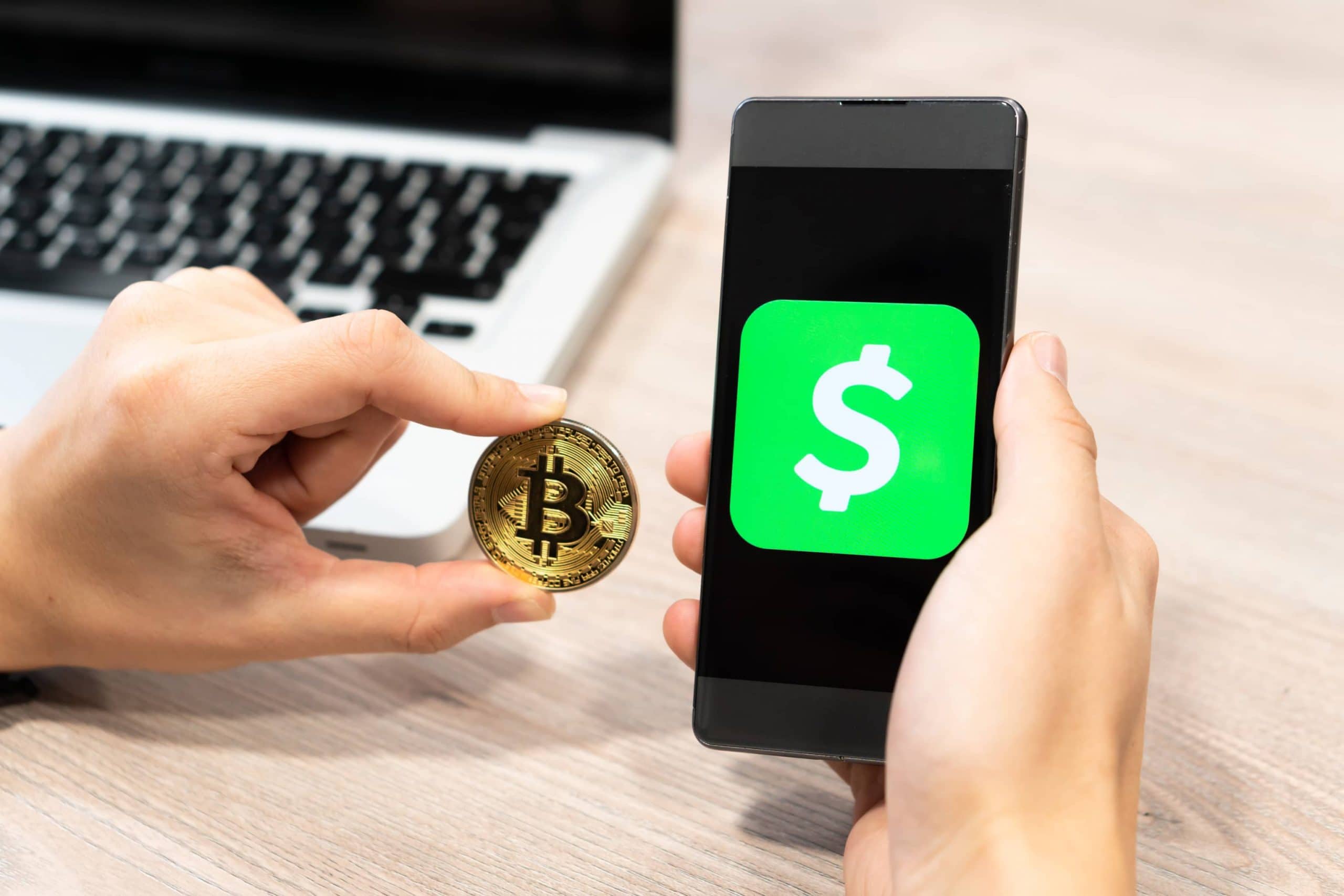 Ein Mann hält eine Bitcoin-Münue neben ein Smartphone, auf dem das Logo der CashApp zu sehen ist.