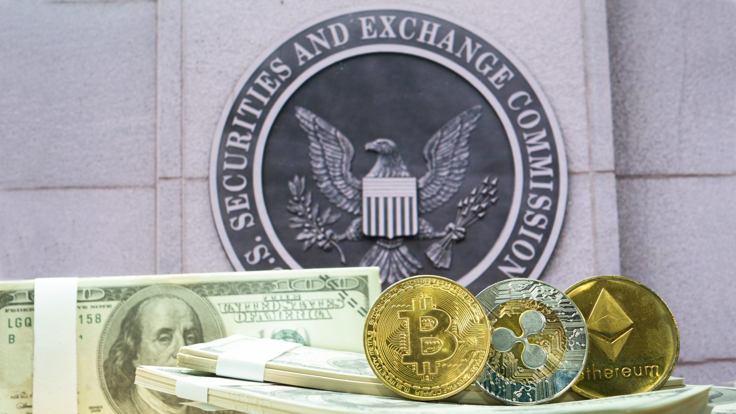 Dollar-Noten, Bitcoin-, Ripple- und Ethereum-Coin vor dem Logo der SEC