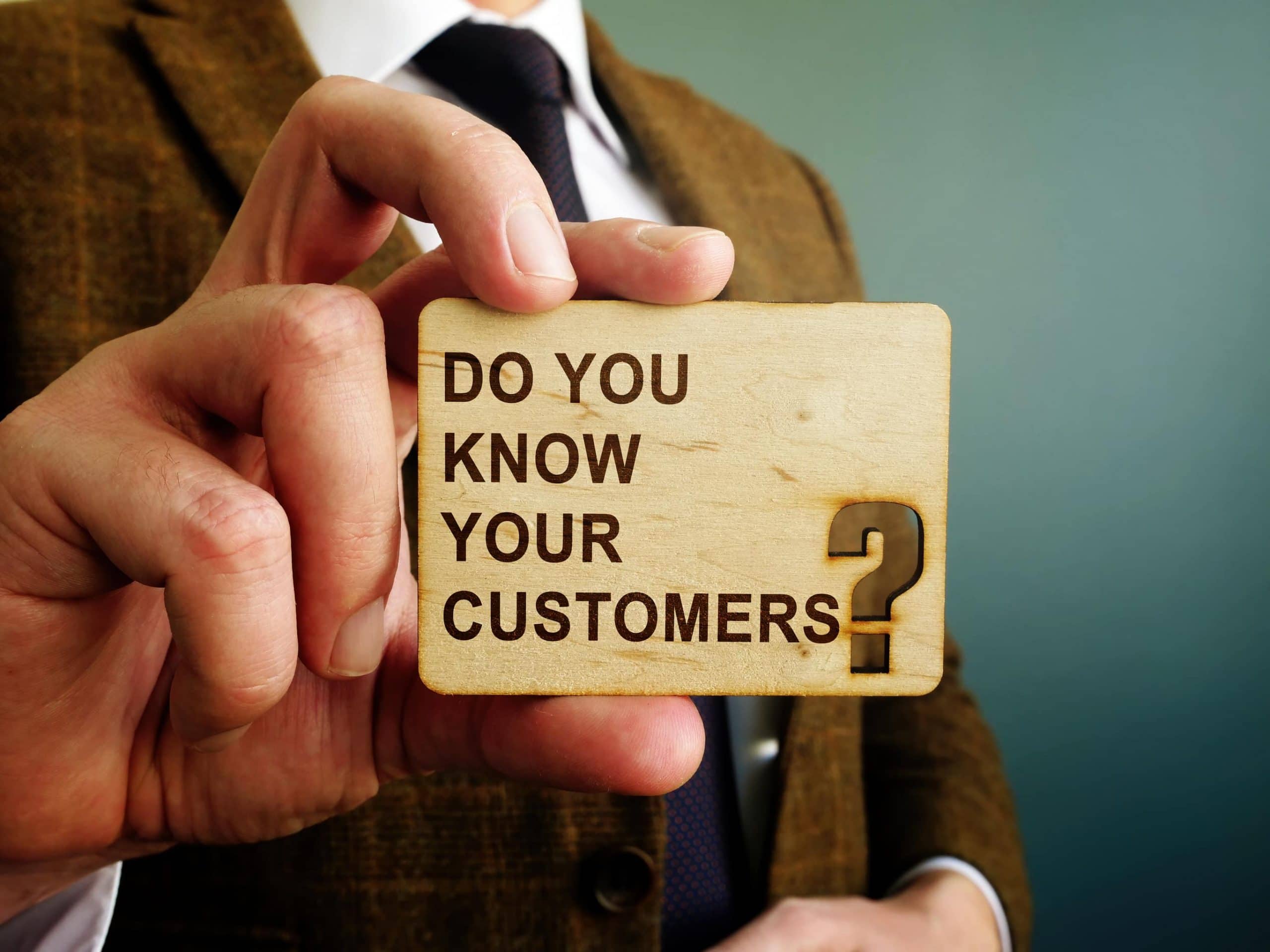 KYC: Ein Mann im Anzug hält ein Schild mit der Aufschrift "Do you Know your Customer?"