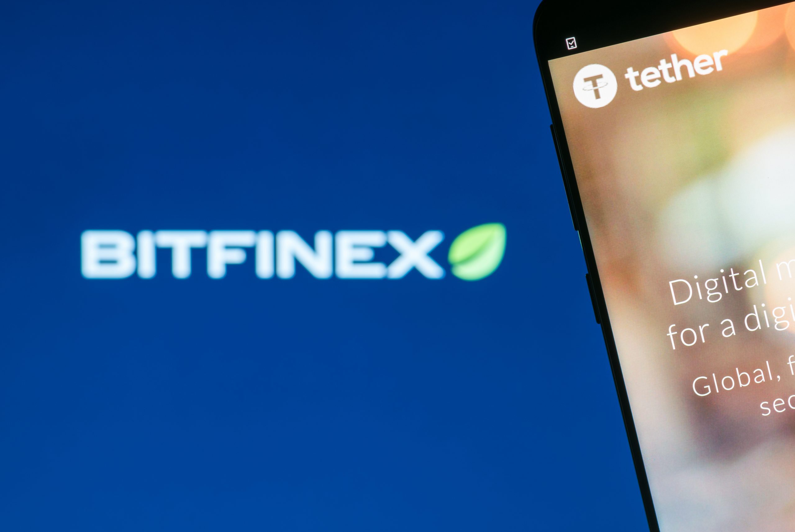 Tether-Logo auf einem Cmartphone vor Bitfinex-Logo