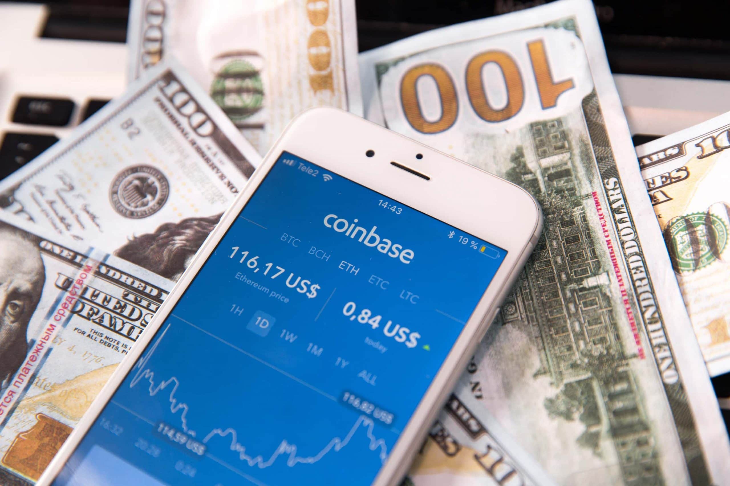 Ein Smartphone-Bildschirm mit geöffneter Coinbase-App liegt auf mehreren Geld-Noten